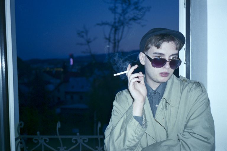 A boy smoking a cigarette in front of an evening window