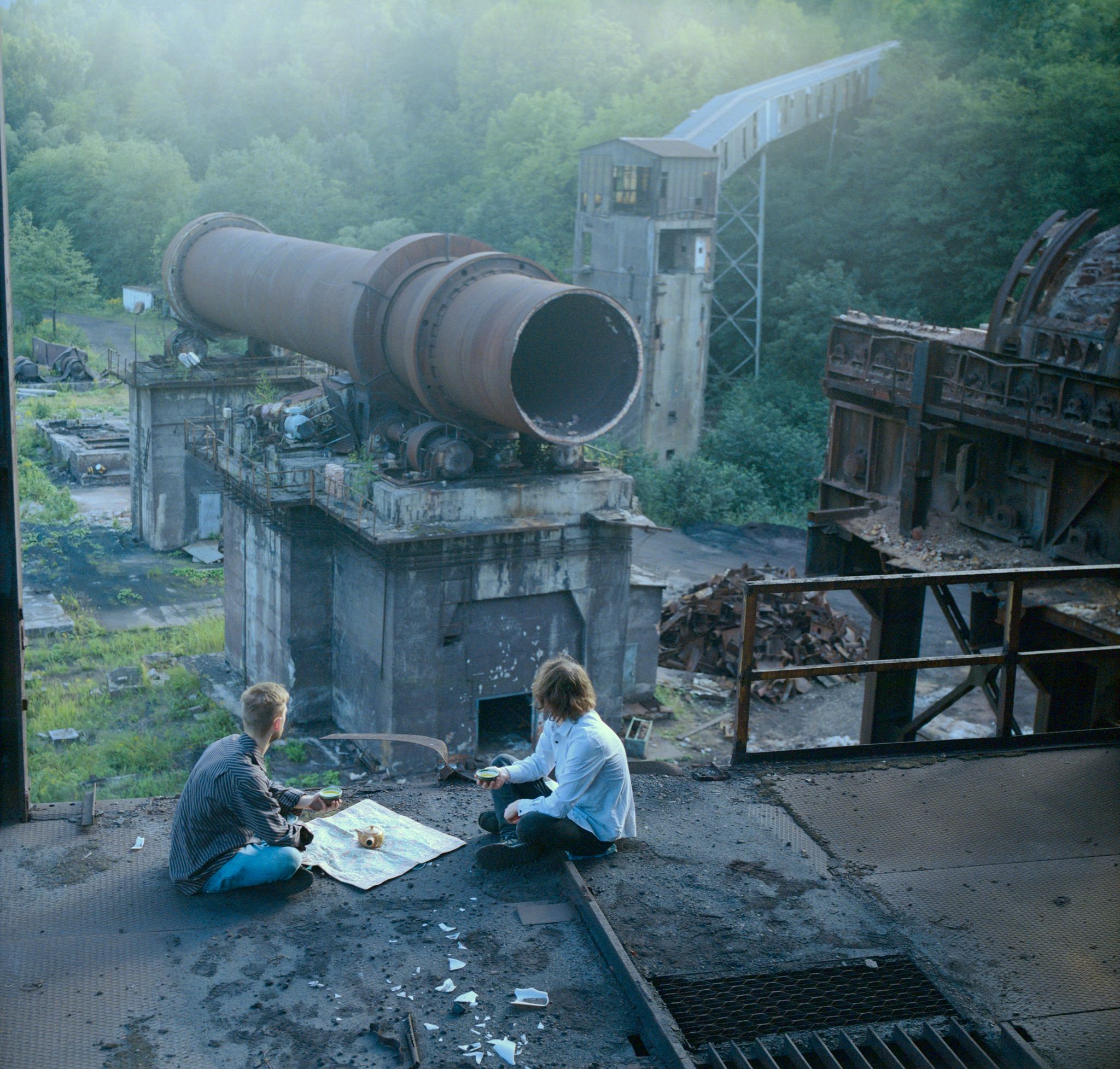 Two boys drinking tea in front of a derelict furnace