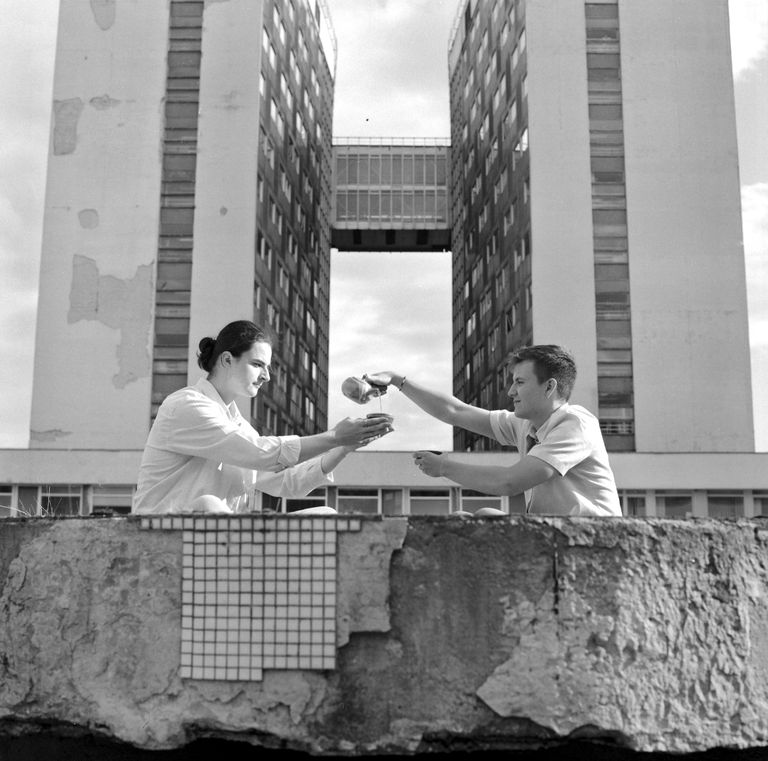Two boys drinking tea together in front of a derelict hospital